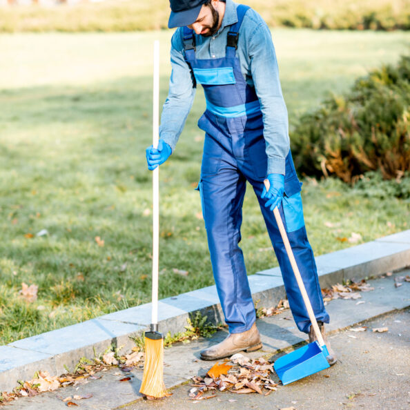 Professional sweeper in uniform sweeping leaves with broom and scoop on the street